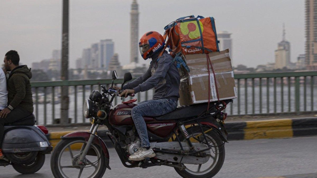A soft delivery bag visibly deformed under a load of stacked boxes on a motorcycle